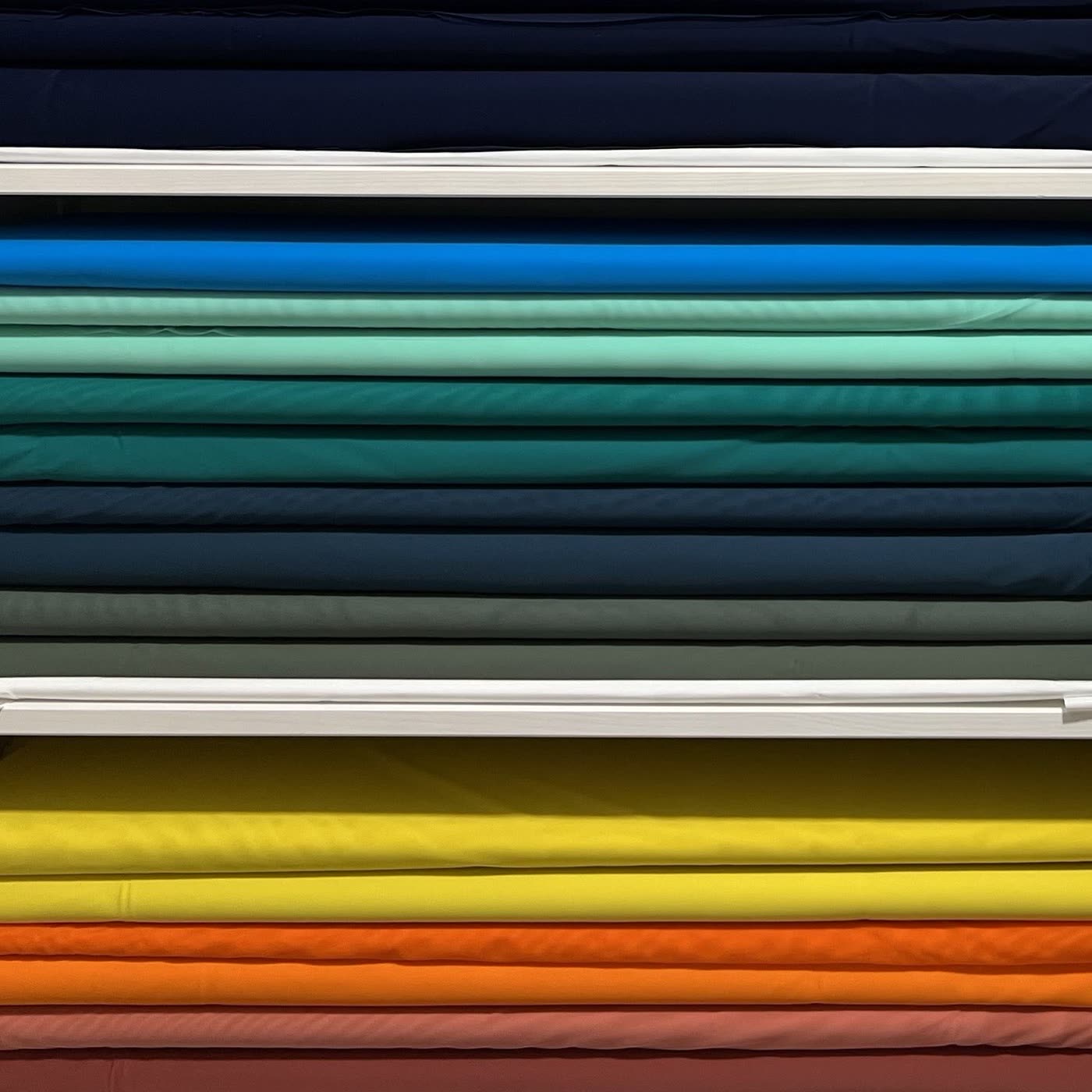 Bolts of stretch costume fabric stacked by colour on the studio shelves